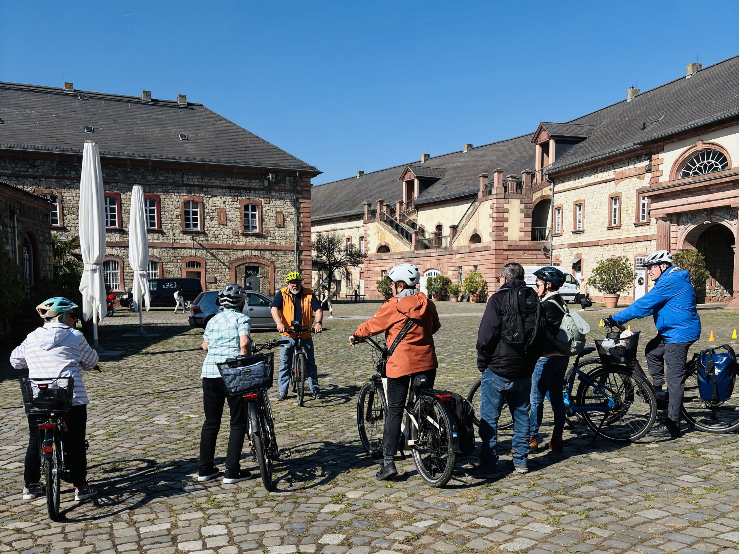 PedelecKurs4_3 Eine im Innenhof der Reduit stehende Gruppe Radfahrer mit Pedelecs im Halbkreis bei Sonnenschein.
