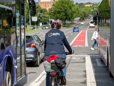 Radfahrerin auf Radfahrstreifen zwischen Bussen und Autos.