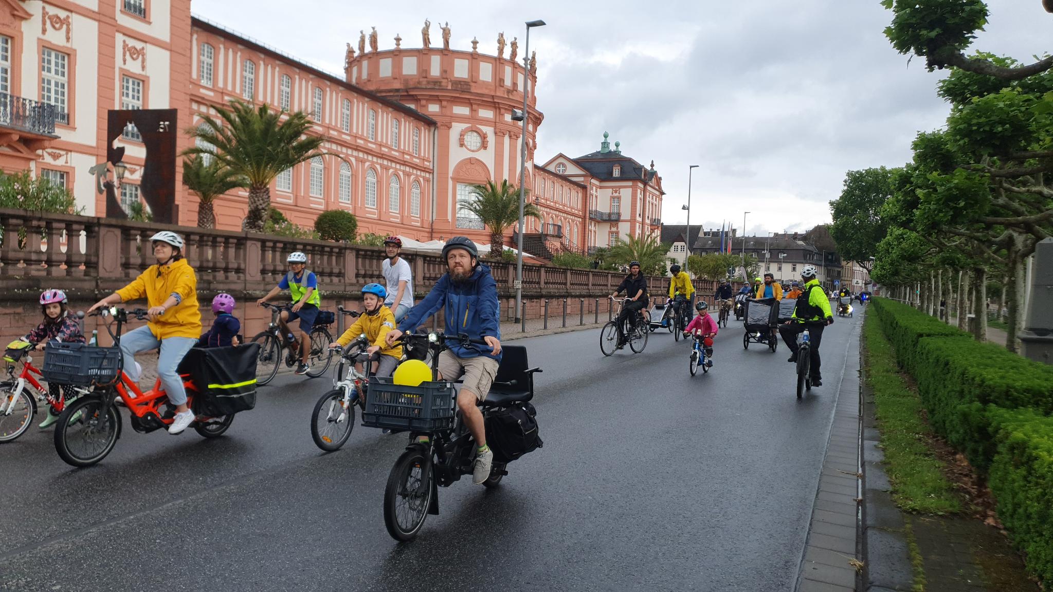 Radelnder Kinder und Erwachsene, teils in Regenbekleidung, vor dem autofreien Biebricher Schloss.