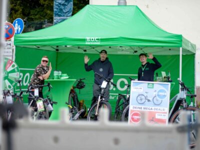 Männer winken vom Stand des Fahrradladens B.O.C.